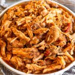 Shredded salsa pork chops on a plate sitting on a towel. Behind it is a jar of seasoning.