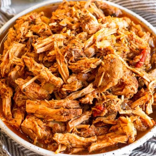 Shredded salsa pork chops on a plate sitting on a towel. Behind it is a jar of seasoning.