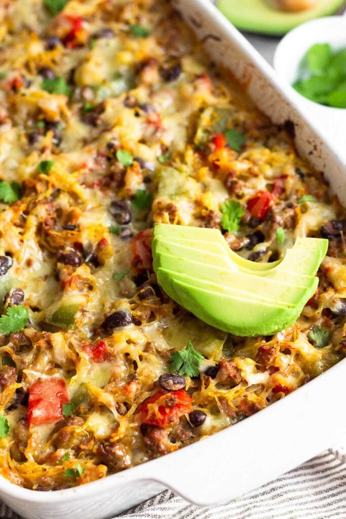 Healthy spaghetti squash casserole with ground meat and veggies in a large baking dish. It is topped with avocado.