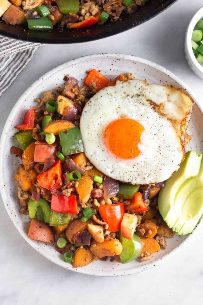 Chicken hash on a plate topped with a fried egg and avocado.