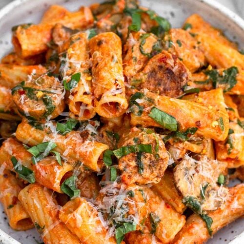Chicken sausage pasta on a plate topped with basil and parmesan cheese.