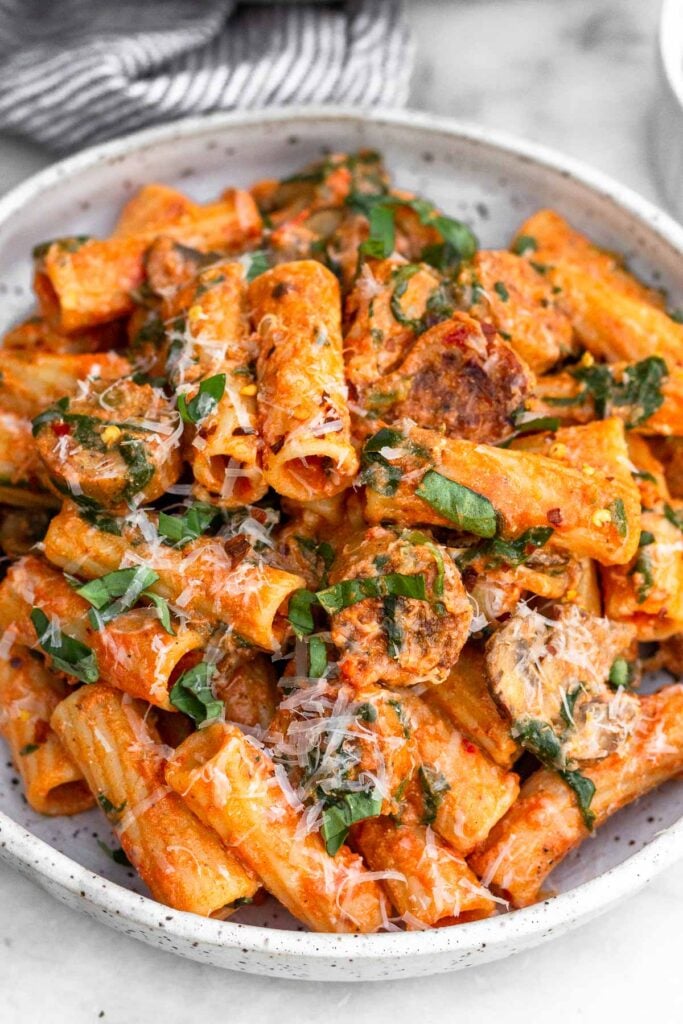 Chicken sausage pasta on a plate topped with basil and parmesan cheese.