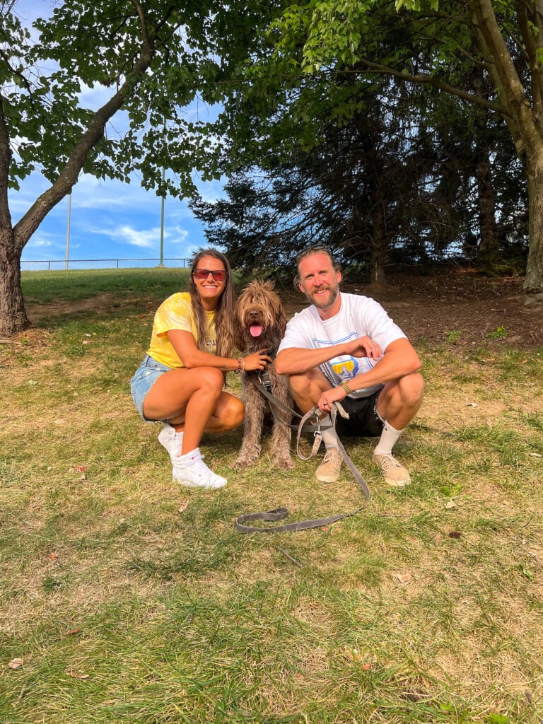 Husband, wife, and their dog sitting on a hill.