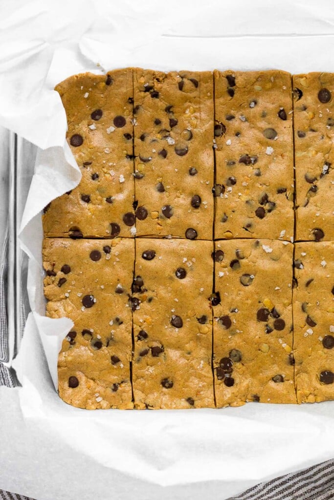 Glass baking dish lined with parchment paper filled with peanut butter chocolate chip protein bars cut into 8 equal bars.