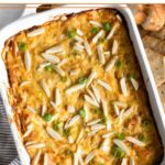 Hot crab dip in a small casserole dish topped with green onions and slivered almonds. Around is it sliced bread and crackers.