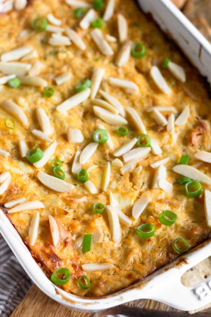 Close up of hot crab dip topped with slivered almonds and green onions.