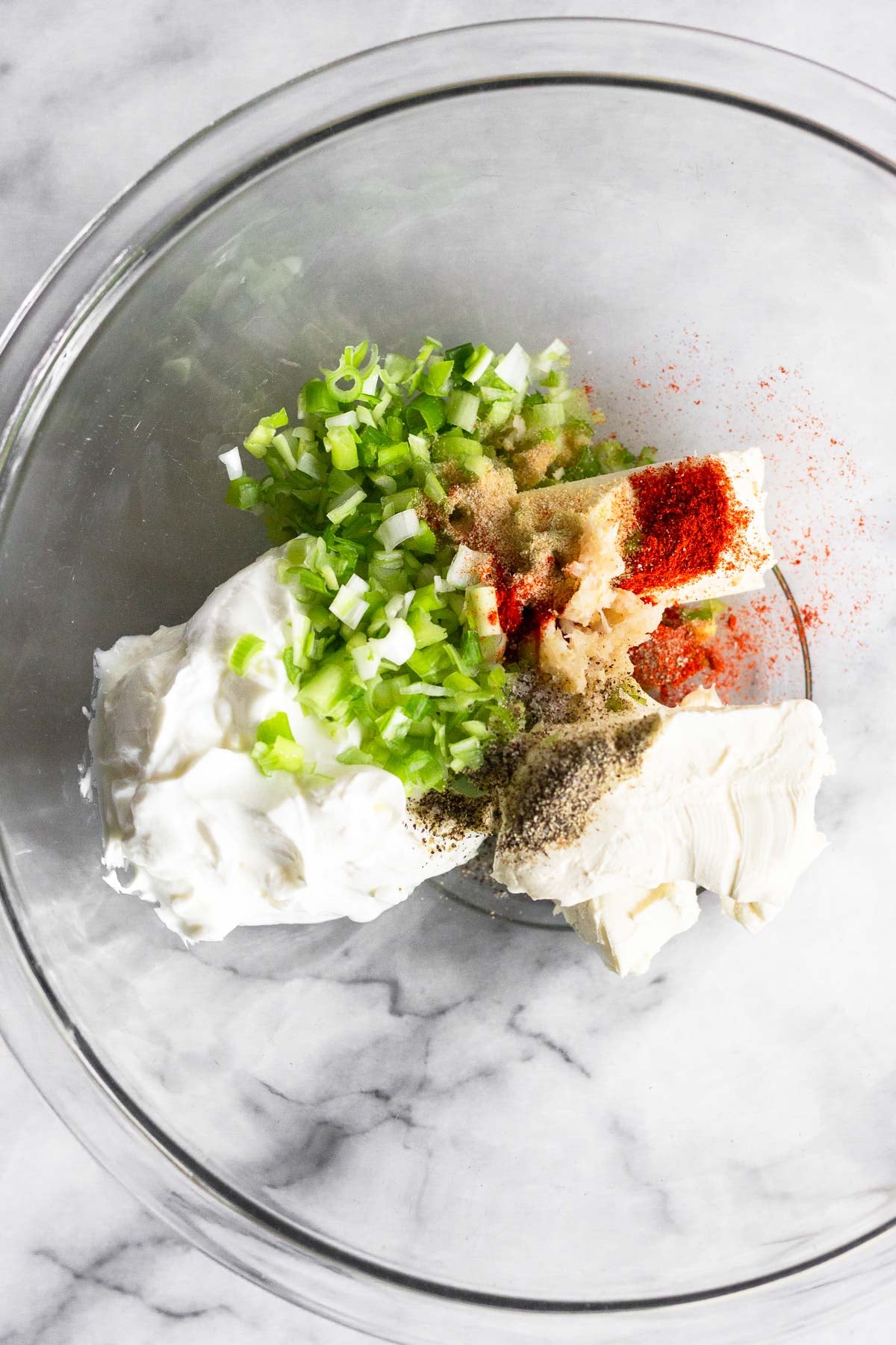 Glass bowl with cream cheese, greek yogurt, minced green onions, and spices.