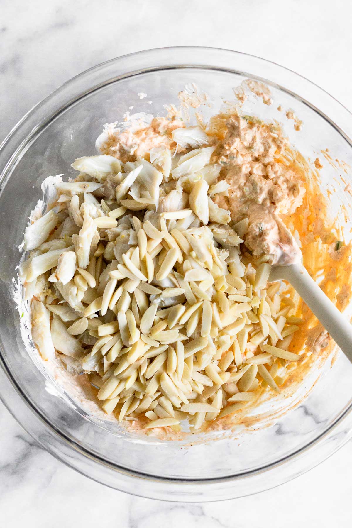 Bowl with a mixture of cream cheese, yogurt, and spices with lump crab and slivered almonds on top.