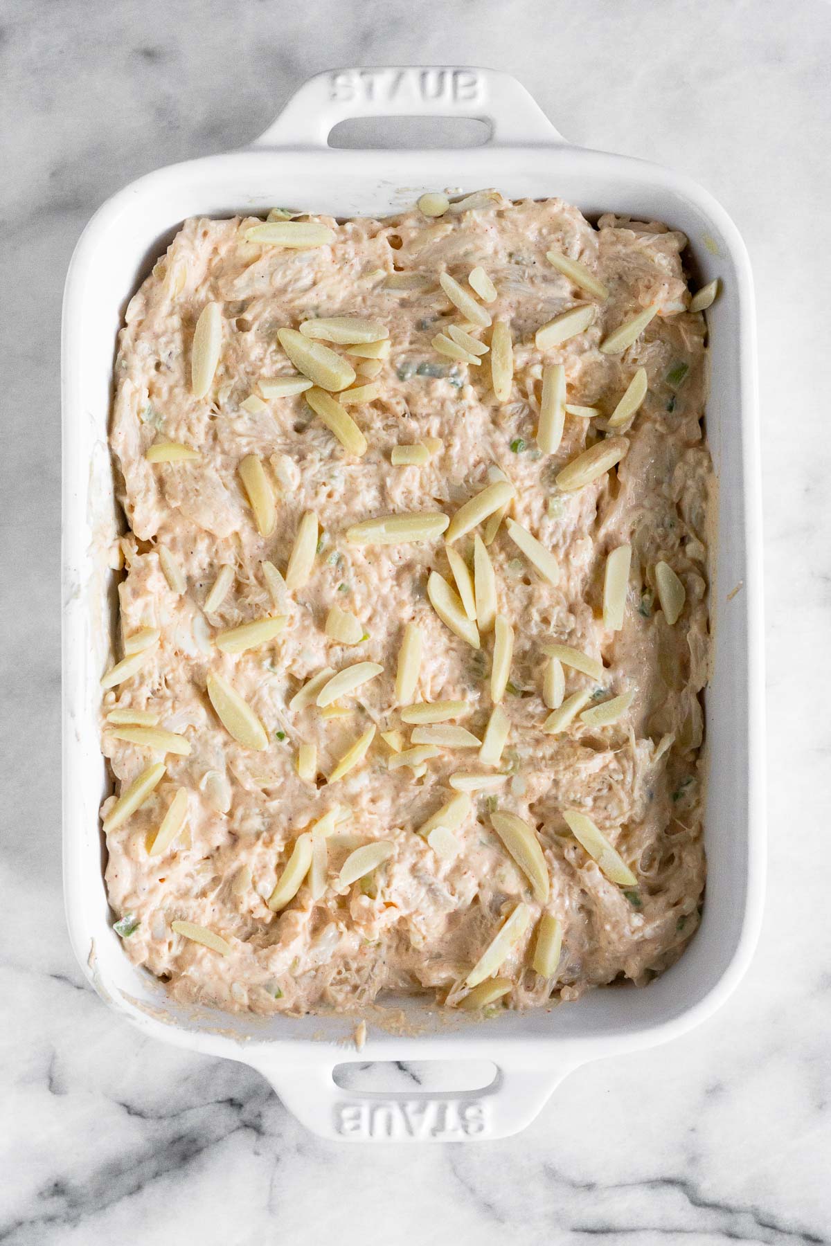 Small casserole dish with crab dip with slivered almonds on top before it is baked.
