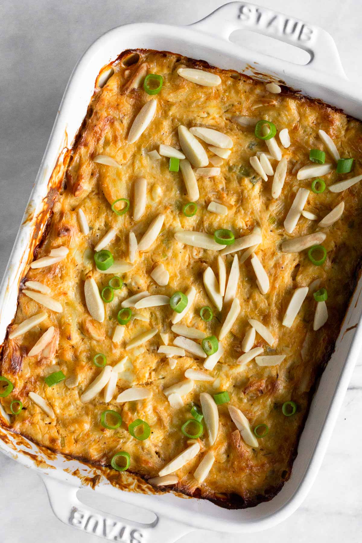 Warm crab dip in a small casserole dish topped with slivered almonds and sliced green onions.