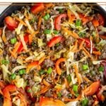 Ground beef and cabbage stir fry in a large cast iron. It is garnished with green onions and sesame seeds.