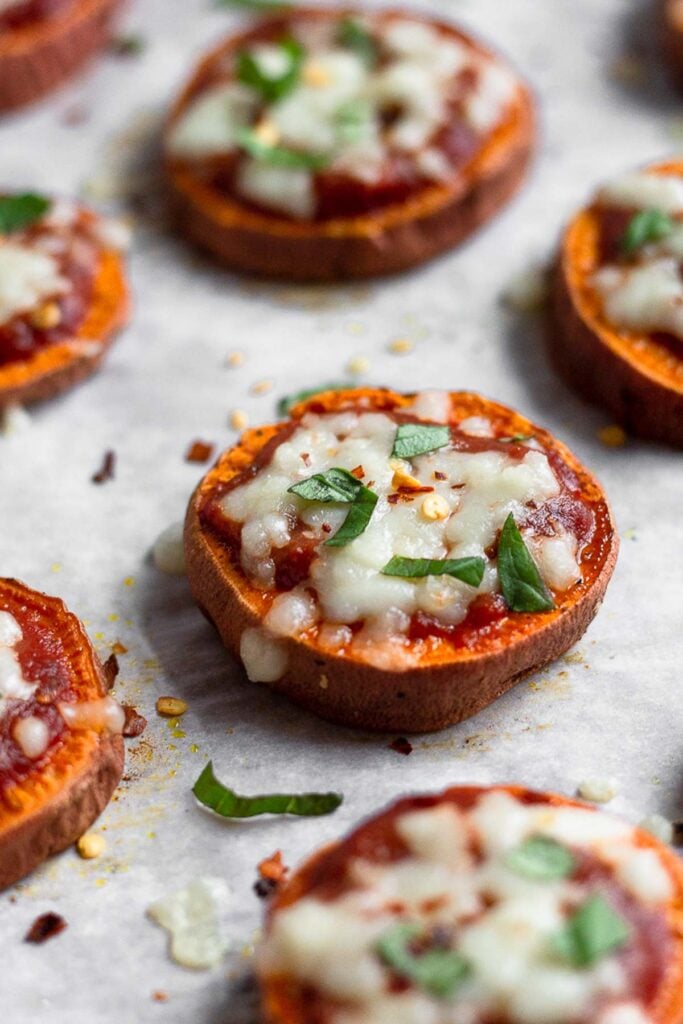 Sweet potato rounds topped with pizza sauce, melted cheese, and basil on a baking sheet.
