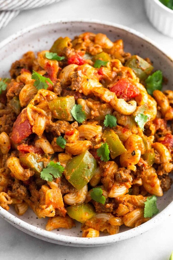 A close up of a plate of taco pasta topped with ground beef and veggies. It is topped with cilantro.