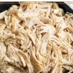 A close-up of a black bowl filled with shredded chicken sprinkled with pepper.