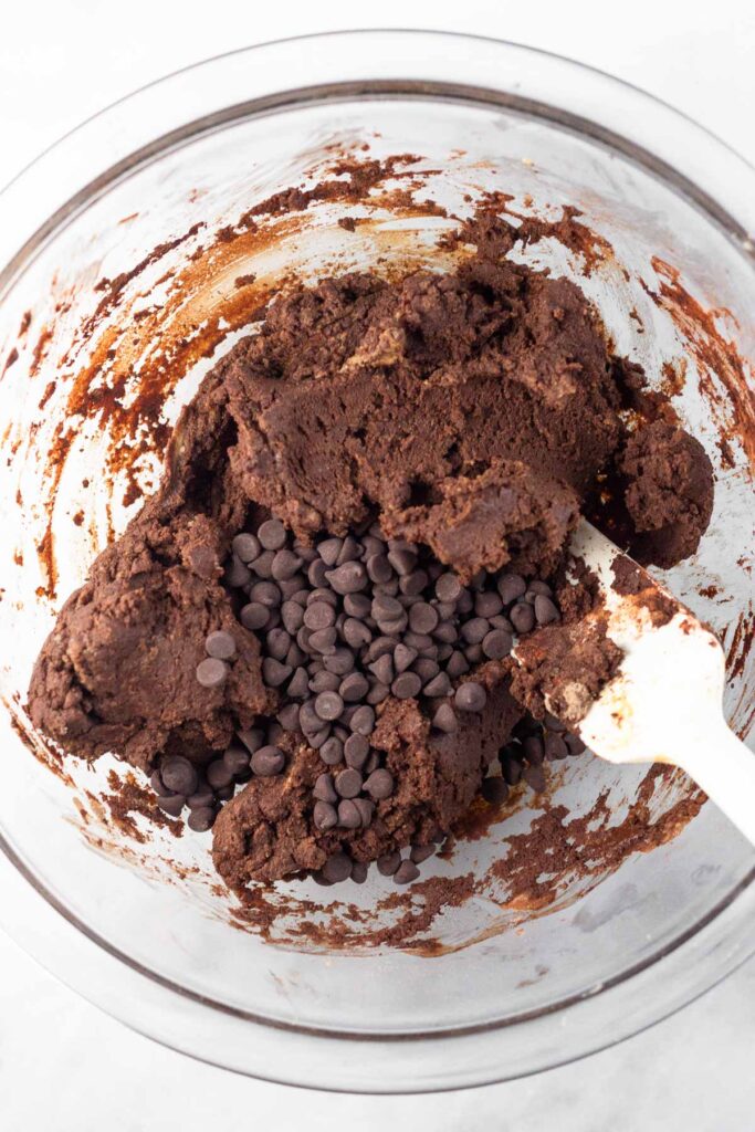 Chocolate protein bar recipe batter with chocolate chips sprinkled on top before it is mixed together in a large glass bowl.