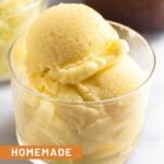 Scoops of pineapple dole whip in a small glass cup. Behind it is another cup and a bowl of frozen pineapple.