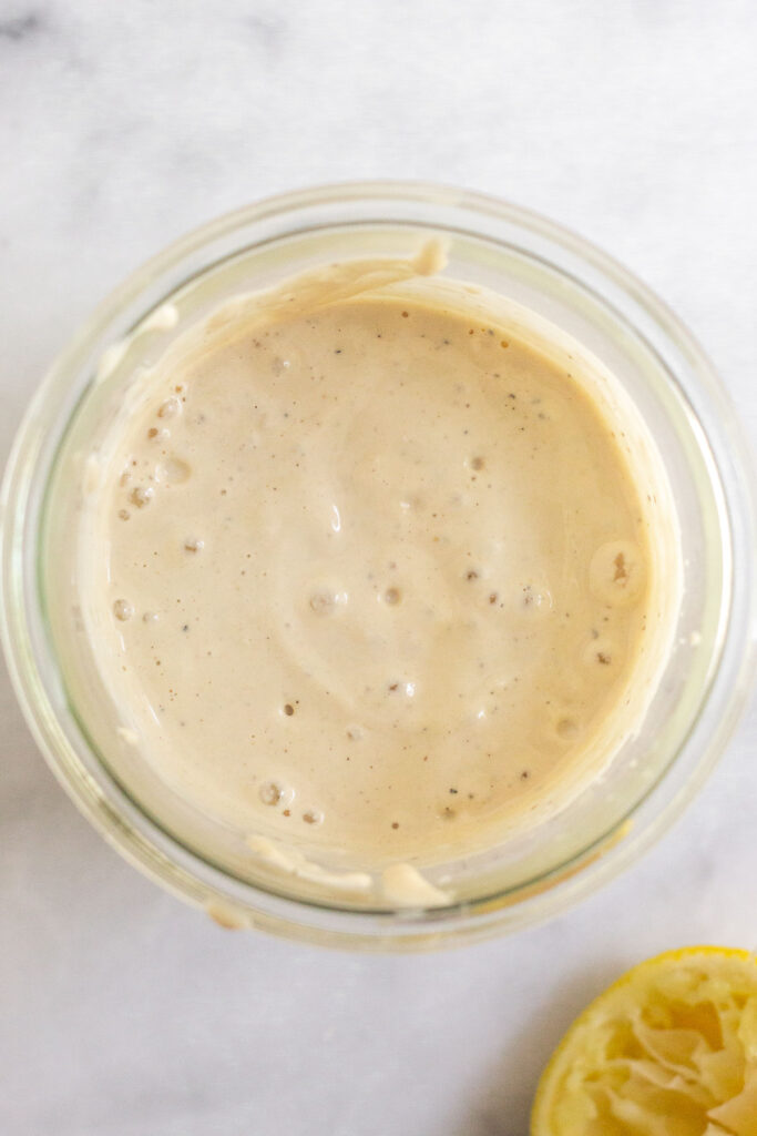 A jar of homemade caesar salad dressing. Next to is it a half a juiced lemon.