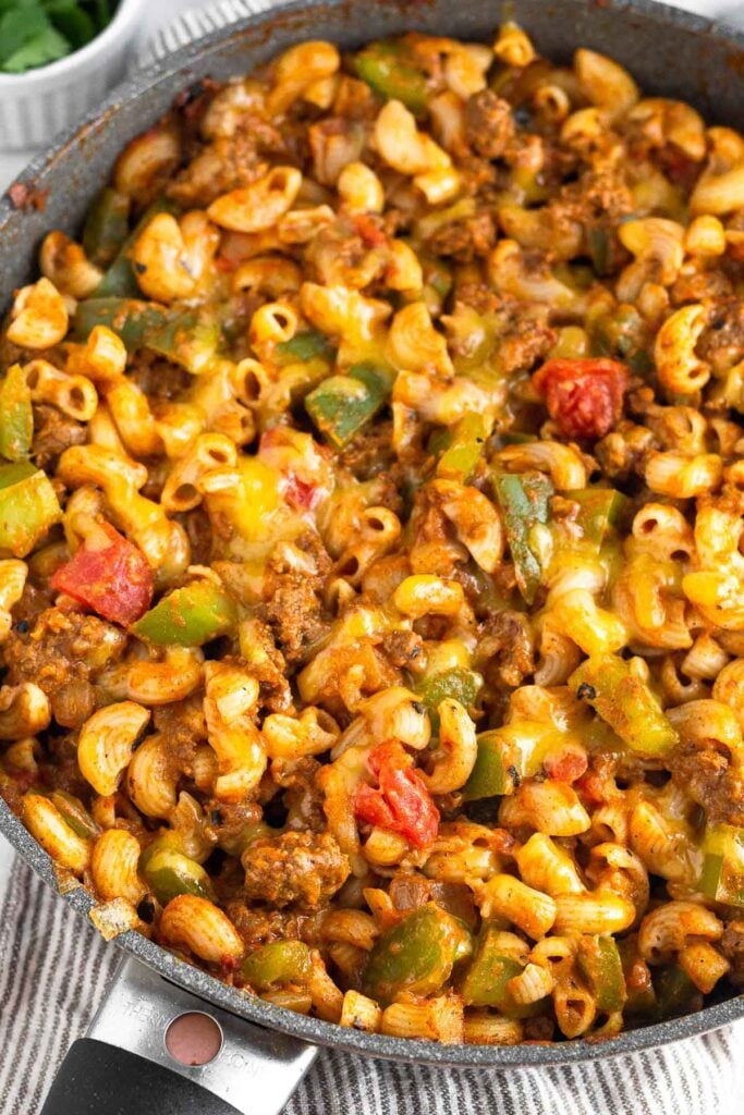 High protein pasta recipe with beef, elbow pasta, veggies, red sauce, and melted cheese on top in a large skillet.