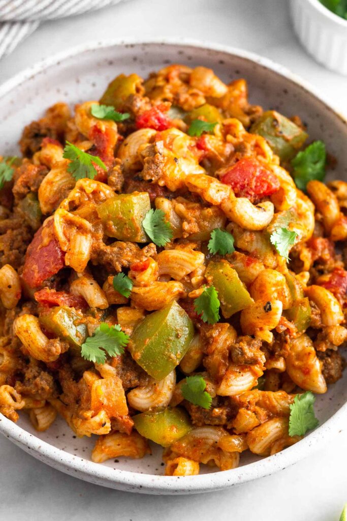 A plate of taco pasta topped with ground beef and veggies. It is topped with cilantro.