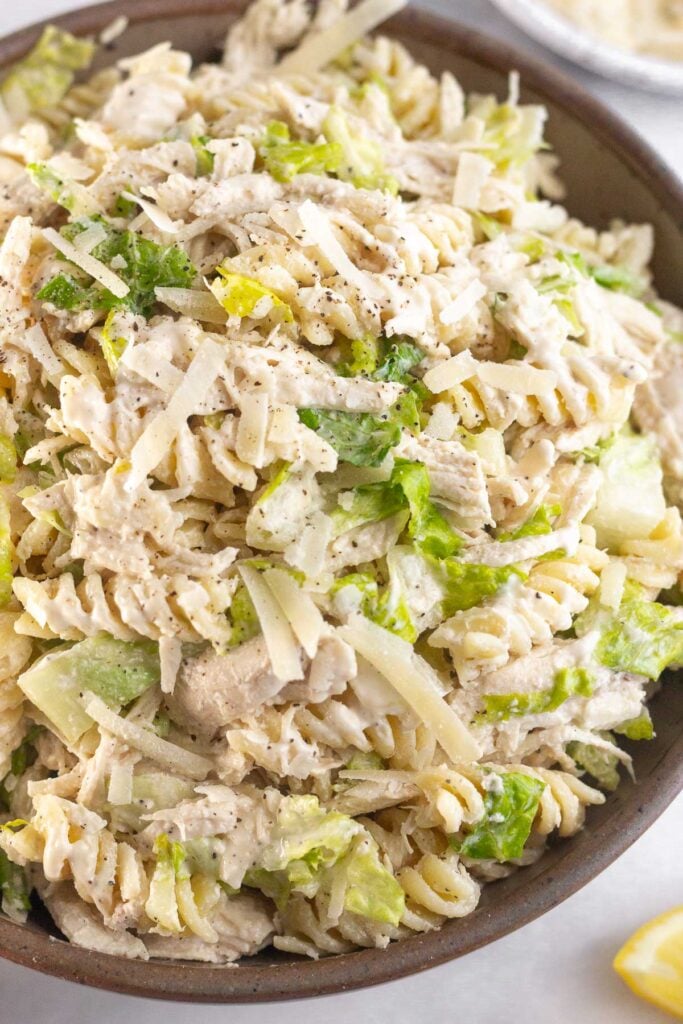 Chicken pasta salad in a large brown bowl. It is garnished with black pepper.
