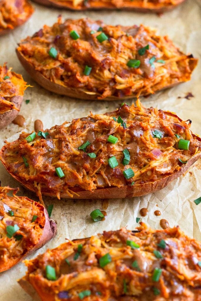 Twice baked sweet potatoes stuffed with shredded BBQ chicken topped with green onions on a baking sheet.