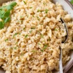 Close up of a bowl of cheese rice garnished with cilantro. A spoon is also in the bowl.