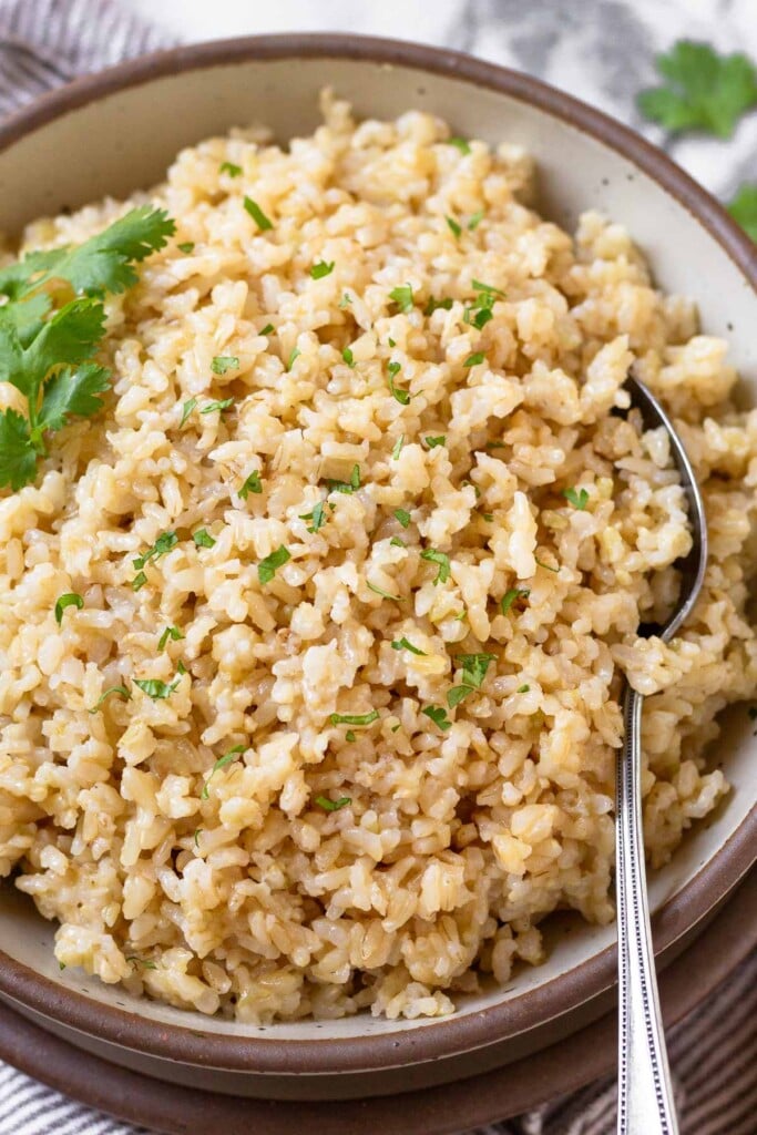 Close up of a bowl of cheese rice garnished with cilantro. A spoon is also in the bowl.