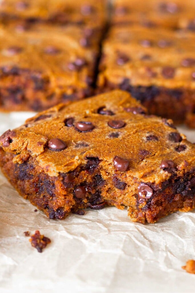Close up a a pumpkin chocolate chip bar with a bite taken out of it. Behind it are more bars lined up.