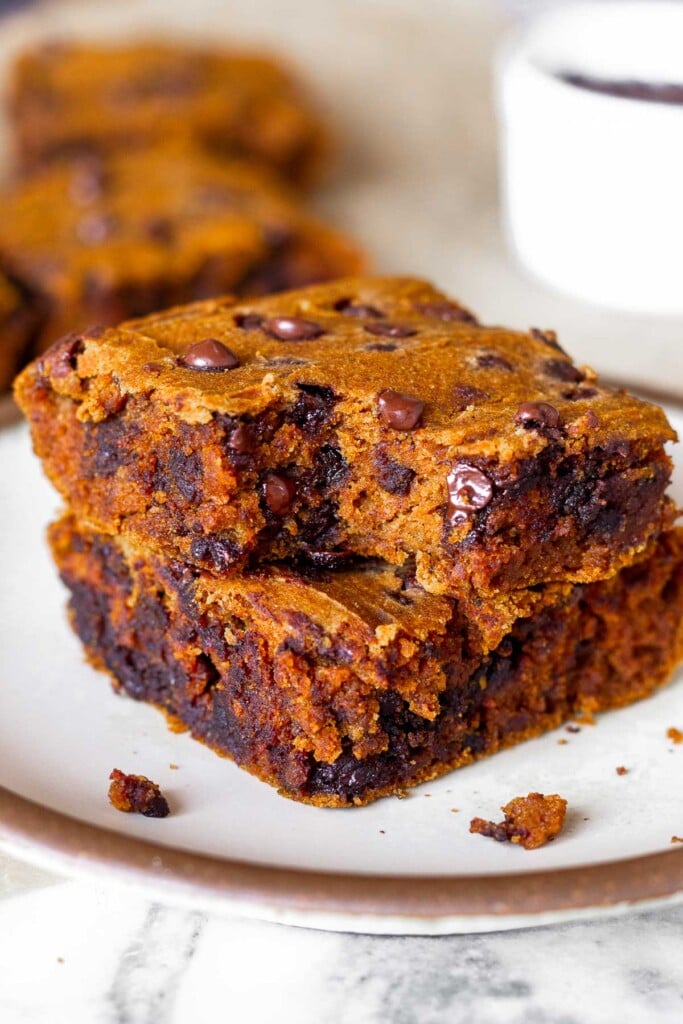 A small plate of two gluten free pumpkin bars stacked on top of each other with a bite taken out of the top one. Behind the plate is more jars and a small white dish.
