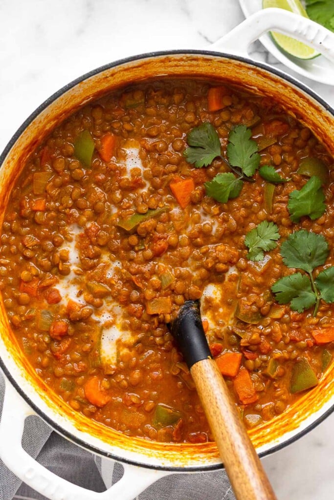 Curry lentil soup in a large pot with a spoon coming out of it. It is topped with cilantro.