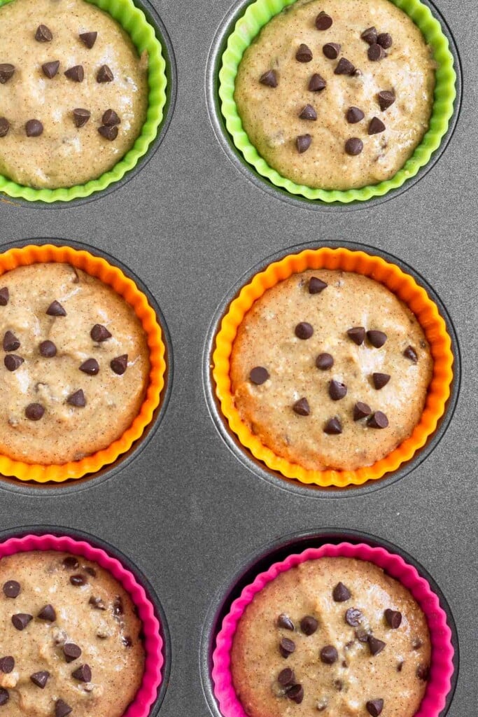 Muffin tin filled with uncooked chocolate chip muffins in it.