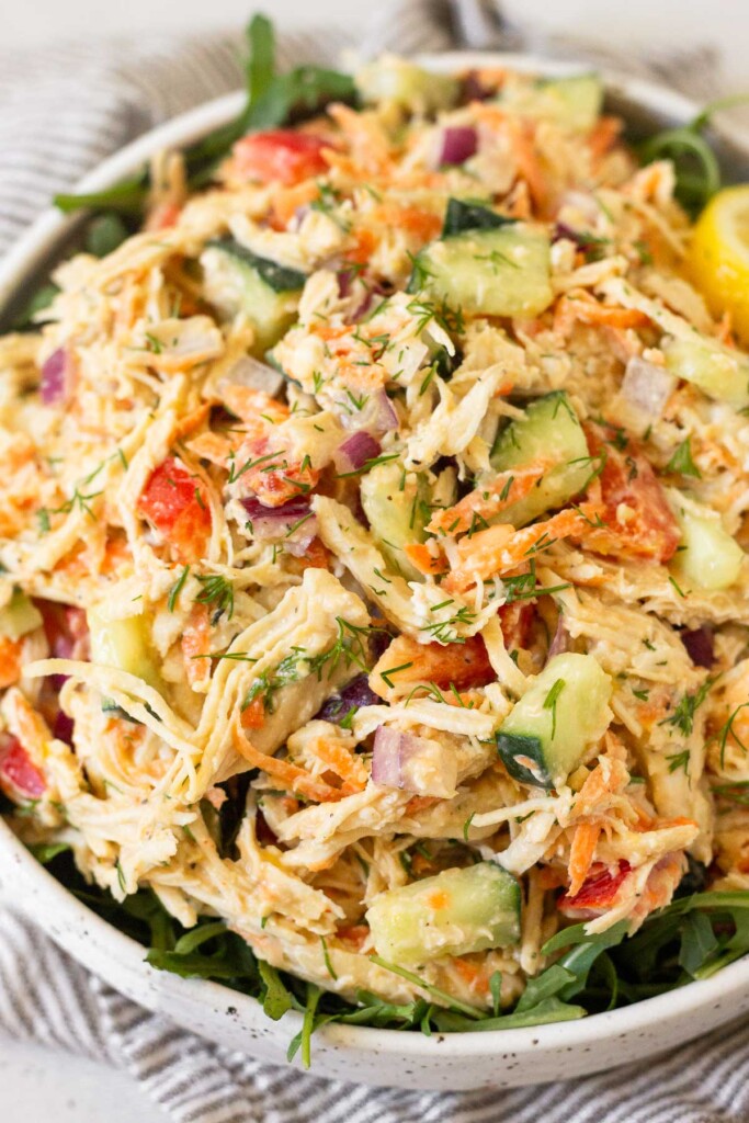 Hummus chicken salad overtop greens in a white bowl.