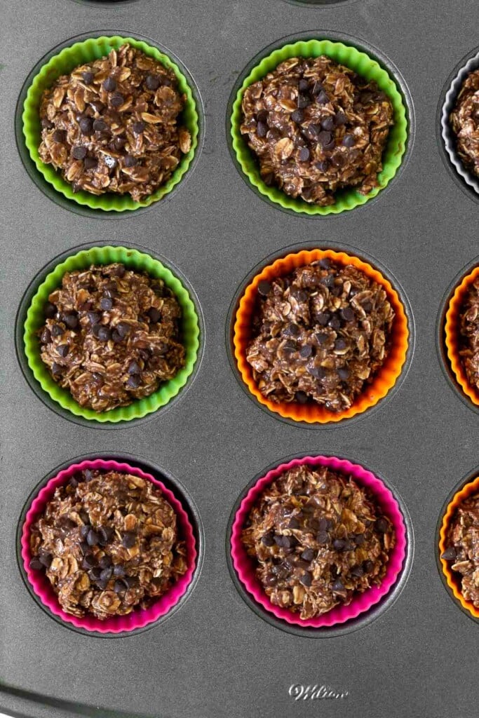 Muffin tin filled with colorful silicon liners with chocolate oatmeal banana muffins muffins in them before they are baked.