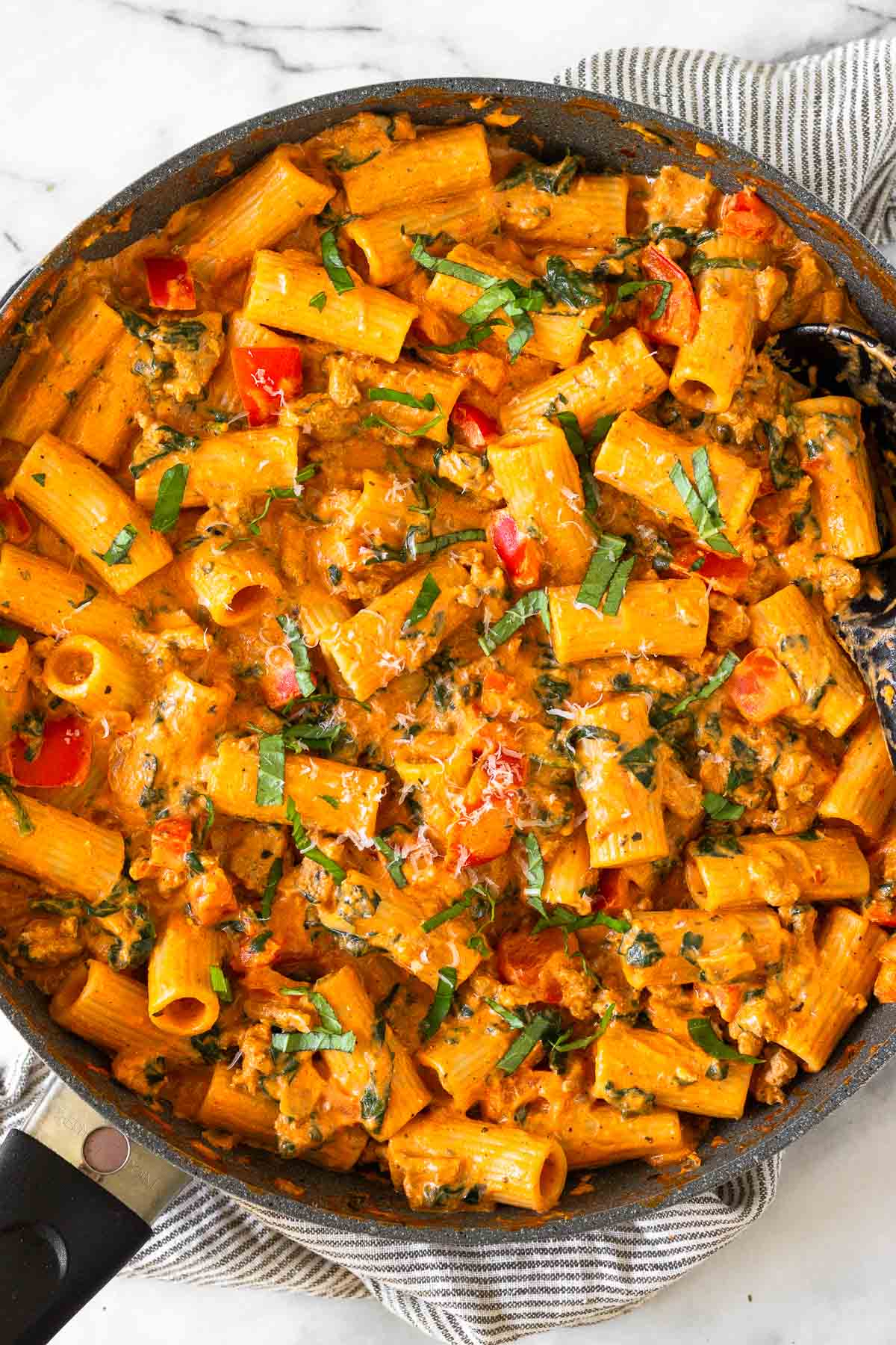 Cottage cheese pasta with ground turkey and veggies in a large skillet garnished with basil and parmesan cheese. The skillet is on top of a striped towel.