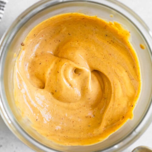 Overhead shot of chipotle mayo in a jar. Next to the jar is a striped towel, a spoon with mayo on it, and a teaspoon.