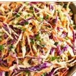 A closeup of a large bowl of healthy coleslaw garnished with fresh cilantro and black pepper.