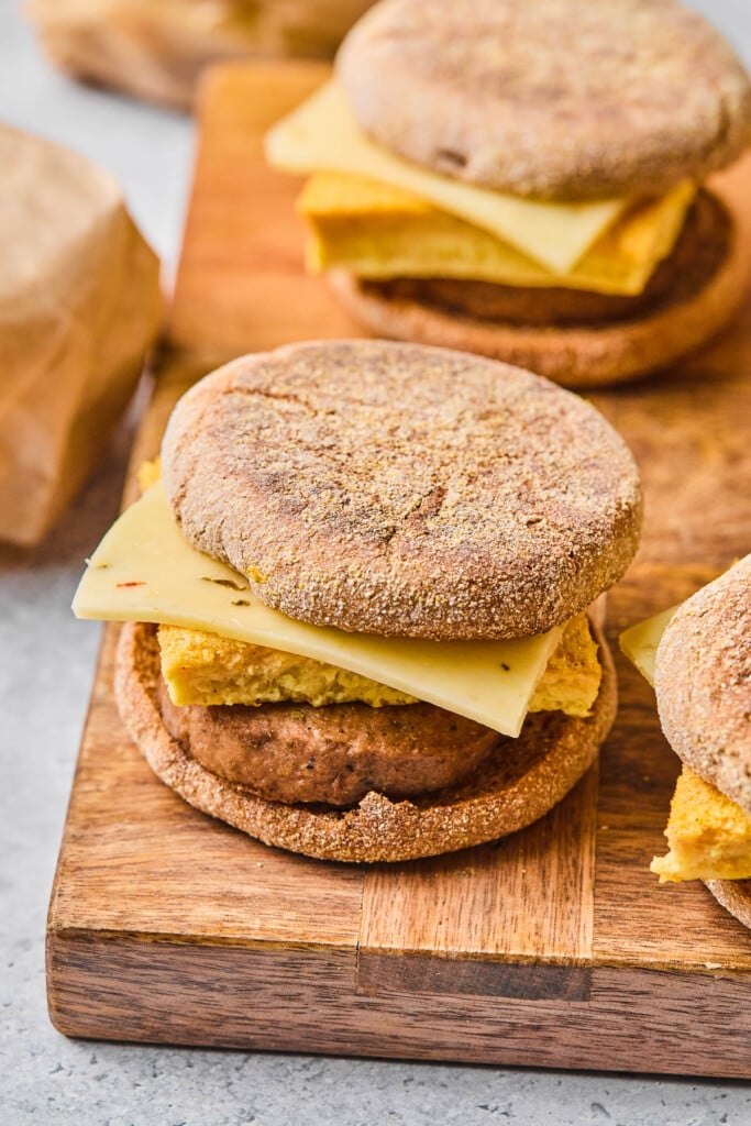 A few high protein meal prep breakfast sandwiches with egg, cheese, and a sausage patty on an English muffin on a cutting board.