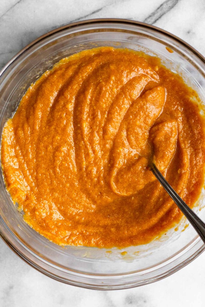 A glass bowl with a wet pumpkin batter with a fork in it.