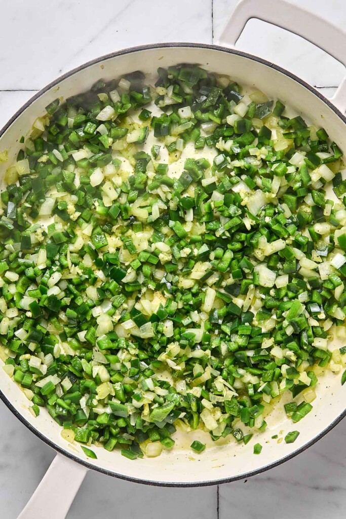 Large white pan with sautéed diced onions and poblano peppers.