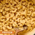 Protein mac and cheese in a large white dutch oven with a wooden spoon in it.