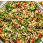 Large bowl filled with Mediterranean farro wiht two wooden salad tongs in the bowl.