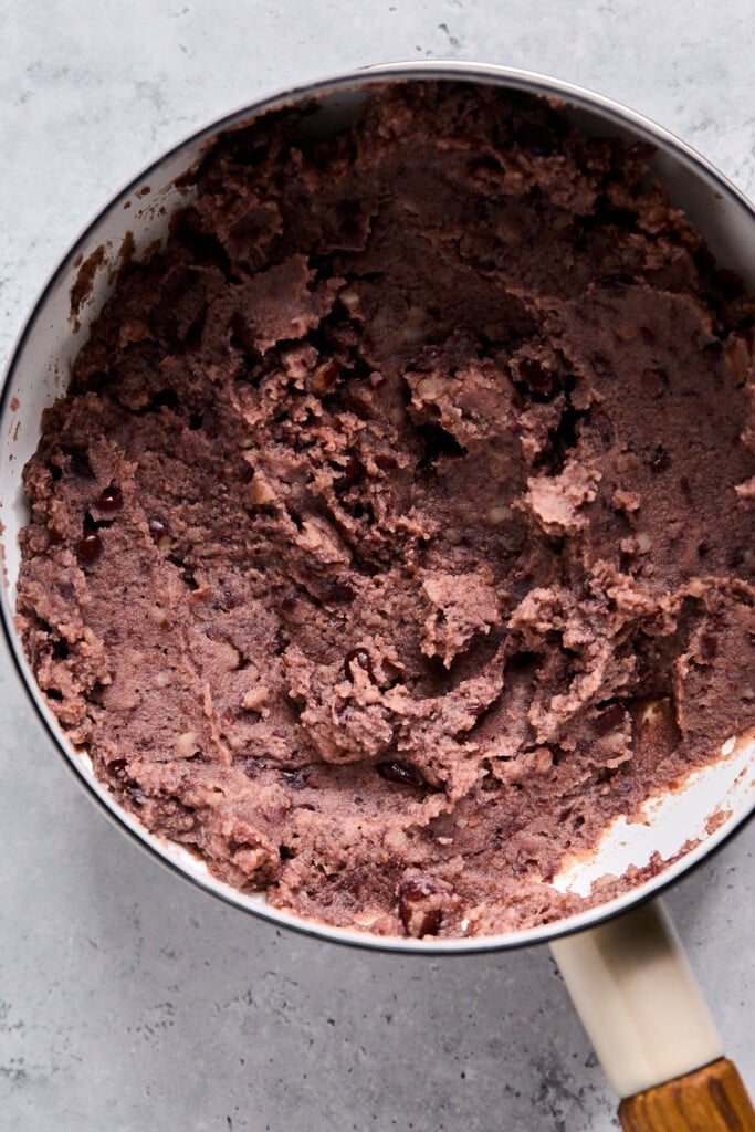 Sauce pan filled with warmed up refried black beans in it.