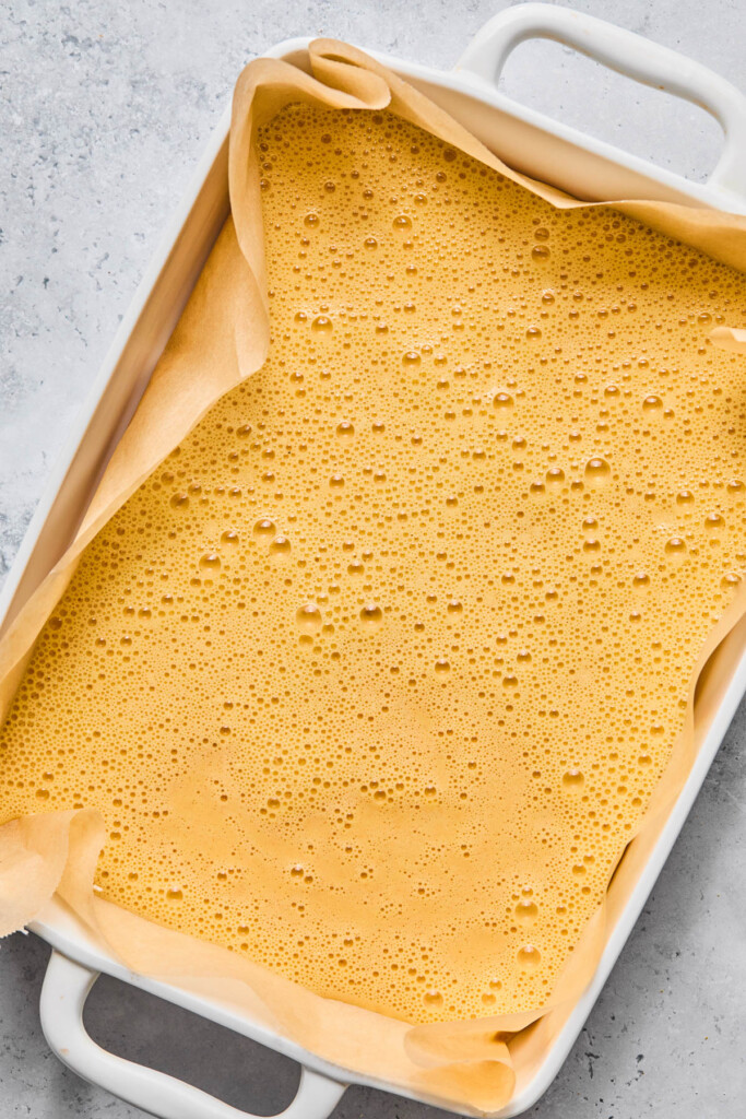 Baking dish lined with parchment paper with a whisked egg mixture in it.