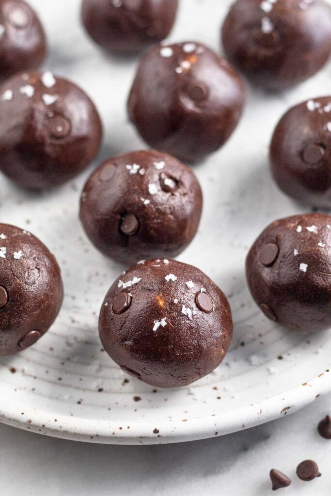 Chocolate protein balls on a white plate. They are sprinkled with sea salt.