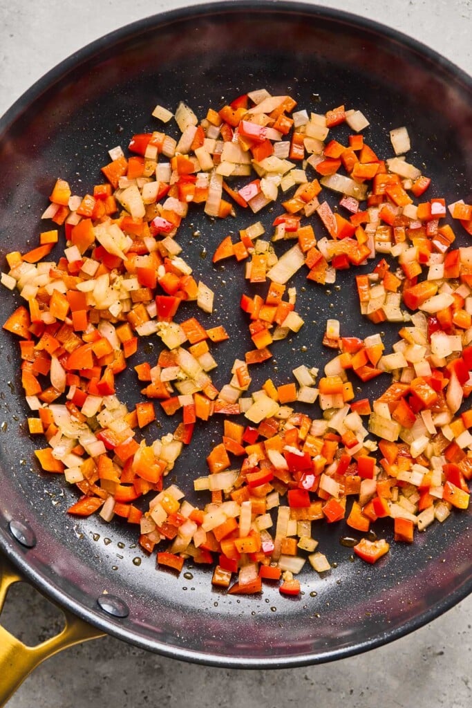 Skillet filled with sautéed diced onions and red bell peppers.