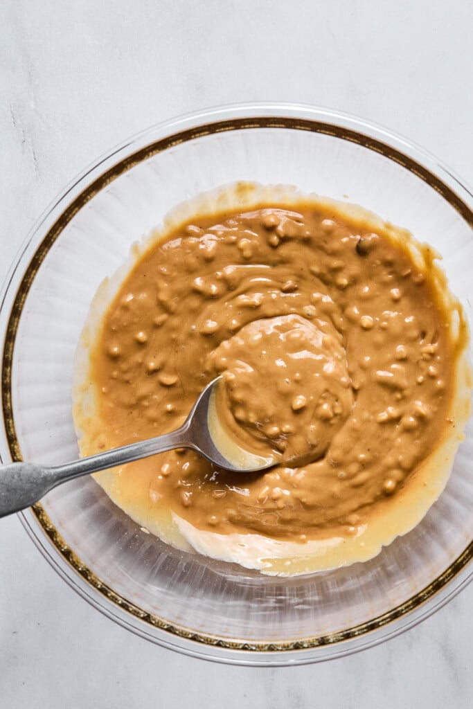 Crunchy peanut butter mixed with a little honey in a glass mixing bowl with a spoon in it.