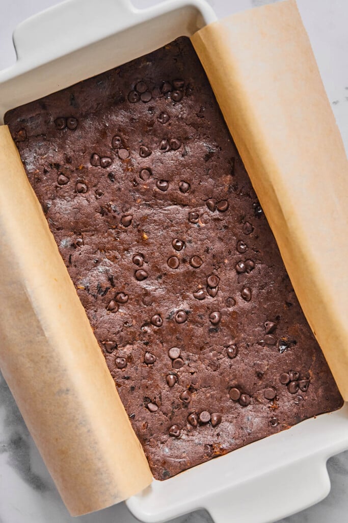 Chocolate dough with chocolate chips pressed into a bread pan lined with parchment paper.