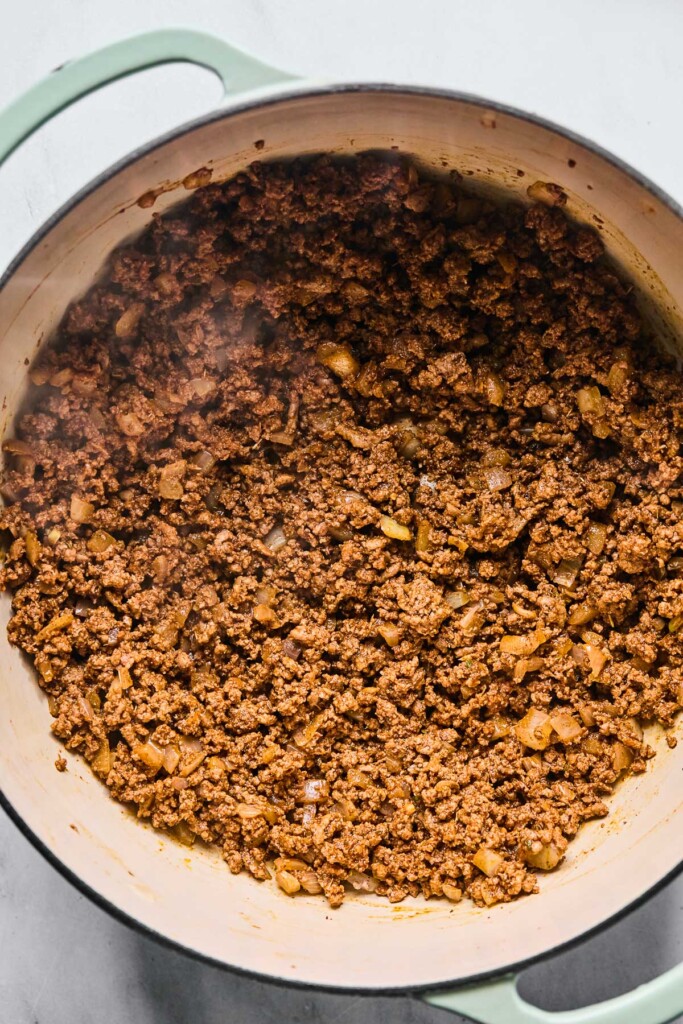 Overhead shot of a large Dutch oven filled with sautéed onions and seasoned ground beef.