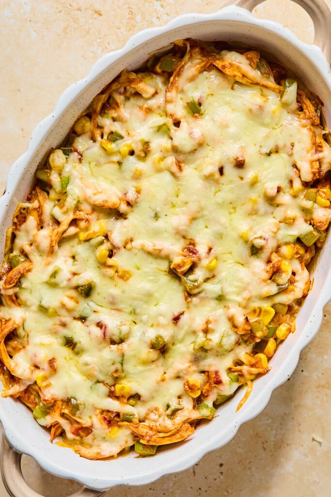 Shredded chicken and veggie dip topped with melted cheese in a white au gratin dish.