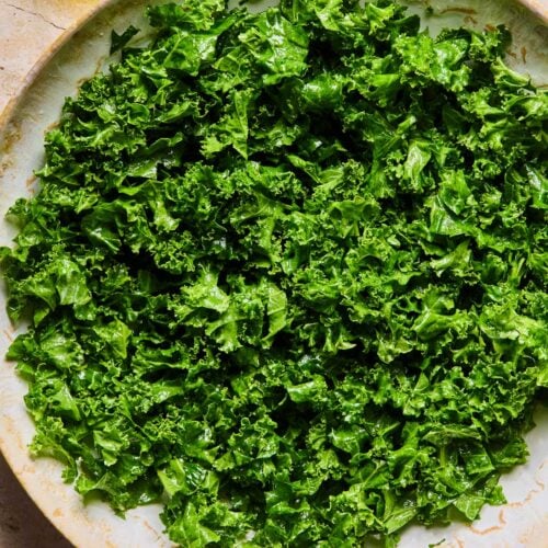 Massaged kale in a large bowl. Next to the bowl is half a juiced lemon and an olive oil cruet. `